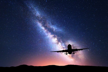 Obraz premium Droga Mleczna i sylwetka samolotu. Krajobraz z samolotem pasażerskim leci w gwiaździste niebo w nocy. Tło. Komercyjny samolot pasażerski na tle kolorowej Drogi Mlecznej. Samolot