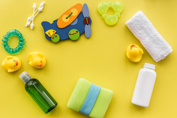 cosmetics for baby bath, towel and toys on yellow background top view space for text