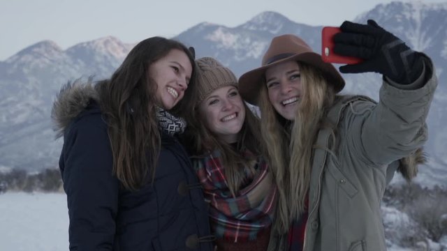 Portrait Of Fun Teen Girls Taking Silly And Cute Selfies Together, With Beautiful Snowy Mountains In Background