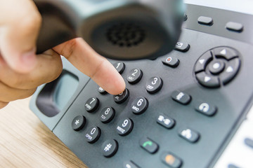 Closeup of male hand holding telephone receiver while dialing a telephone number to make a call...