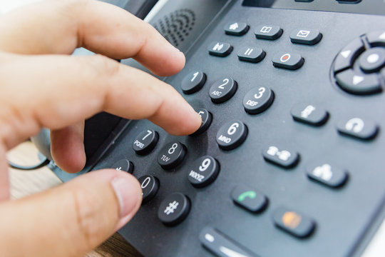 Closeup of male hand holding telephone receiver while dialing a telephone number to make a call using a black landline phone. Conceptual of global communication, business support and customer care.
