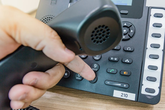 Closeup of male hand holding telephone receiver while dialing a telephone number to make a call using a black landline phone. Conceptual of global communication, business support and customer care.
