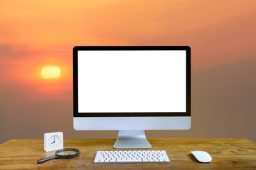 Computer Monitor with white screen, keyboard and mouse with magnifying glass and alarm clock on the wooden table isolated sunset background.