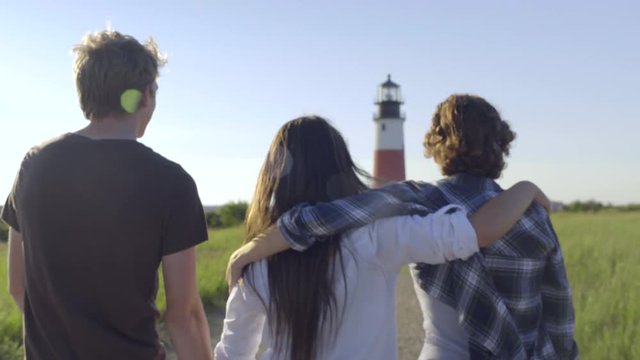 Multiethnic Group Of Excited Friends Walk Toward Historic Lighthouse