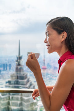 Asian woman enjoying afternoon high tea in luxury cafe or fancy restaurant with city view of Shanghai's landmark skyscrapers in Pudong, China. Chinese tourist lady drinking hot cup of coffee relaxing.