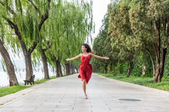 Happy beautiful young woman dancing of freedom in summer park with trees in the background. Asian woman in red dress running of happiness.