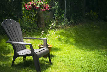 Simple adirondack chair on grassy area with potted plant and hanging basket of flowers