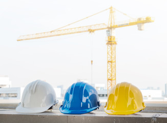 The safety helmet put on the blueprint at construction site with crane background