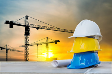 The white safety helmet at construction site with sunset silhouette and crane background
