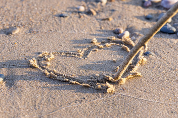 Closeup of heart drawn in sand with branch