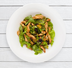 Salad with prunes and fried chicken fillet top view. Healthy food, sport meal, lunch dish concept. White wooden planks background.