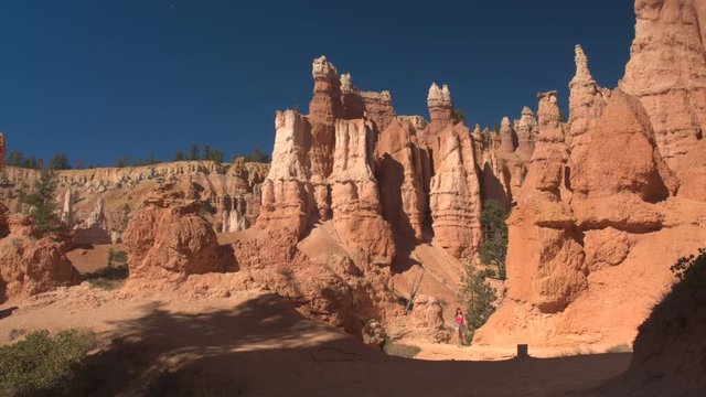 Young woman hiker walking along the empty narrow path exploring majestic hoodoo formations in Bryce canyon national park in sunny Utah