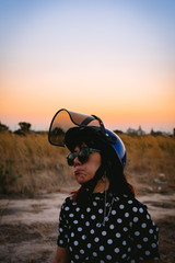 The woman wear polka dot with motorcycle helmet and sunglasses posting near meadow with twilight time.