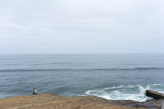 Man sitting alone on Sunset Cliffs in San Diego looking over ocean