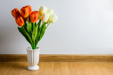 orange, white tulip flowers bouquet in vase on wooden floor in front of cement wall