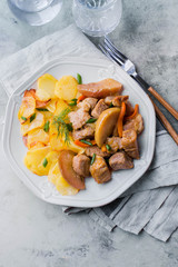 Pork stewed with apples with potatoes for garnish on plate on gray table background. Meat for lunch/dinner