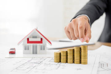 Businessman putting coin on top of money stacks with blurred house model in background