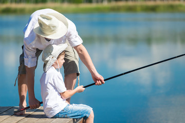 Dad helps his son catch fish with a fishing rod on the river