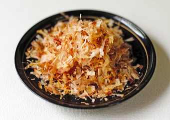 A bowl of katsuo bushi (fish flakes) on a dark dish against a white background. 