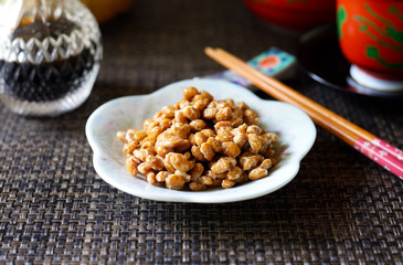 A bowl of natto on a white dish against a dark background.