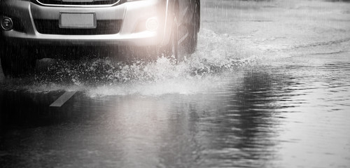 Motion car runs through flood with water splash during hard rain fall.