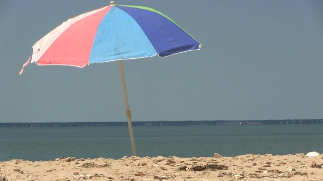 A colorful beach umbrella against blue sky moves in light breeze at south monomoy island Cape Cod