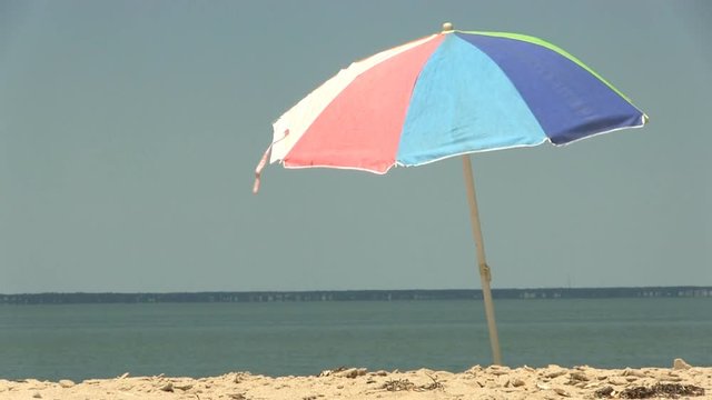 A colorful beach umbrella against blue sky moves in light breeze at south monomoy island Cape Cod