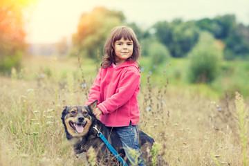 Happy little girl walking with dog on the field