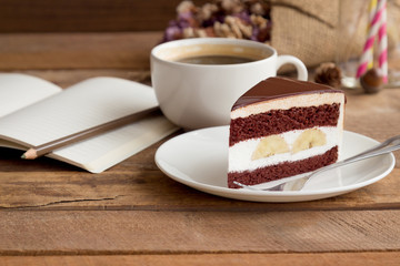 Banana chocolate cake on white plate served with black coffee. Chocolate cake layered with whipped cream and banana look so delicious. Enjoy eating at cafe restaurant with chocolate cake and coffee.