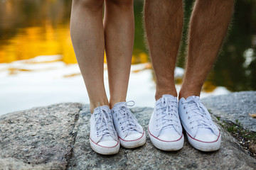 Love story told by boots. Human feet close up. Man and woman in sneakers. Girl in white shoes. Guy in black sneakers and denim. Hipster couple in summer. Legs close up.