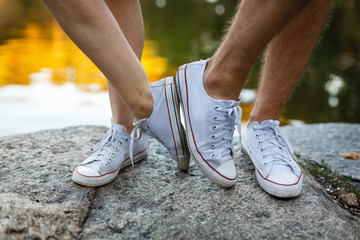 Love story told by boots. Human feet close up. Man and woman in sneakers. Girl in white shoes. Guy in black sneakers and denim. Hipster couple in summer. Legs close up.