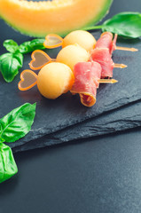 Colorful canape on skewers with melon and prosciutto