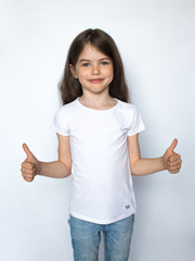 Happy child, little girl showing thumbs up gesture in a white T-shirt isolated on white background. Space for Your Text. Ok sign