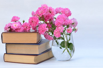 A stack of books and beautiful flowers in a glass vase.