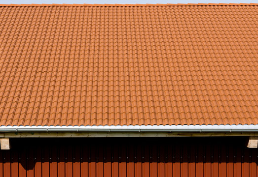 Red tiles roof with rain pipe and corrugated metal wall.