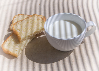 A glass of milk and pieces of white bread. The shadow of the blinds falls on the picture.