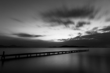 Fototapeta na wymiar Long exposure shot of a pier on a lake, with perfectly still water and moving clouds