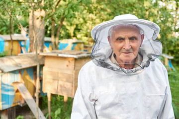 Happy senior man wearing beekeeping suit smiling to the camera posing at his apiary copyspace seniority old profession retirement retired happiness farming.