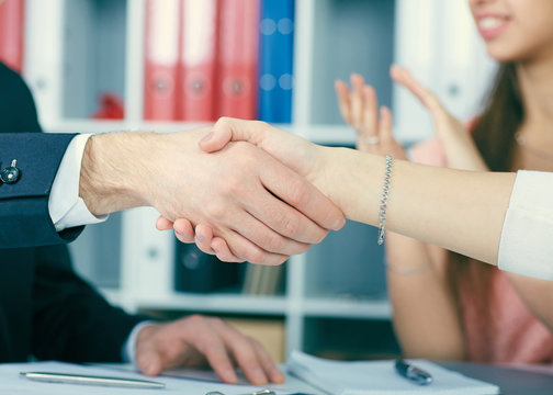 Close up businessmen handshake on team meeting with clapping group of people blured in background at modern startup business office interior.