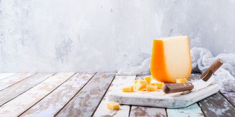 Delicious dutch gouda cheese with cheese cubes and special knife on old wooden table. Copy space.