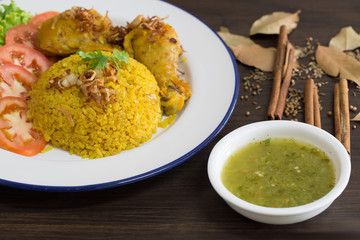 Chicken Biryani on white dish with green sauce (Muslim yellow rice with chicken) on brown wooden background.