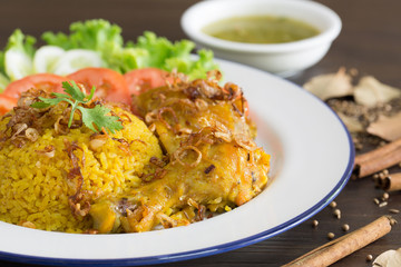 Chicken Biryani on white dish with green sauce (Muslim yellow rice with chicken) on brown wooden background..