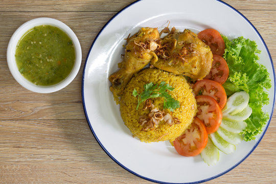 Chicken Biryani on white dish with green sauce (Muslim yellow rice with chicken) on brown wooden background.