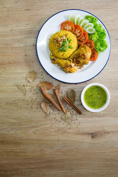 Chicken Biryani on white dish with green sauce (Muslim yellow rice with chicken) on brown wooden background