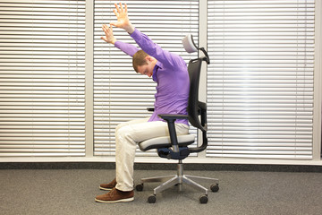 caucasian man stretching arms,exercising on chair in office, healthy lifestyle
