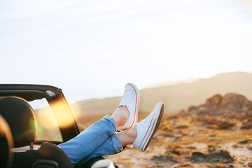 A young woman rests and pushes her shoes out of the convertible to enjoy the view
