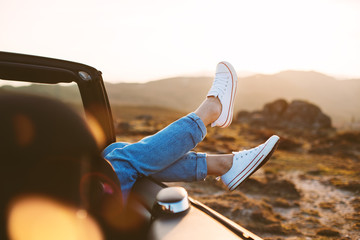 Happy girl rests and pushes her shoes out of the convertible to enjoy the view