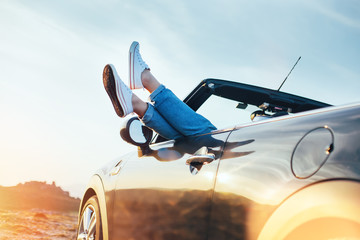 A young woman rests and pushes her sneakers out of the convertible to enjoy the view