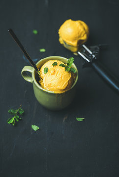 Refreshing summer dessert. Mango sorbet ice cream scoops with fresh mint in green cup over black wooden background, copy space. Clean eating, healthy, vegetarian, dieting, alkaline diet food concept