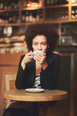 Mixed race business woman taking pause from work and sitting in coffee shop while drinking coffee
